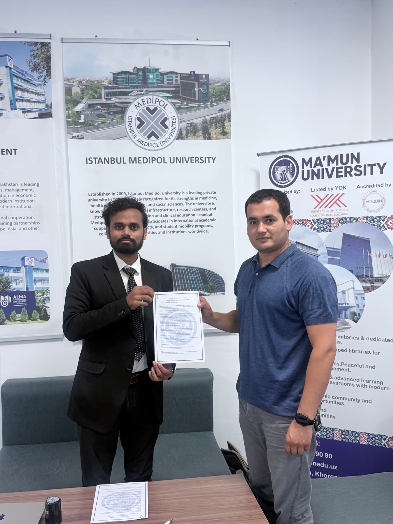 Dr. Ravi holding the signed partnership agreement with a Ma'mun University representative in Uzbekistan.